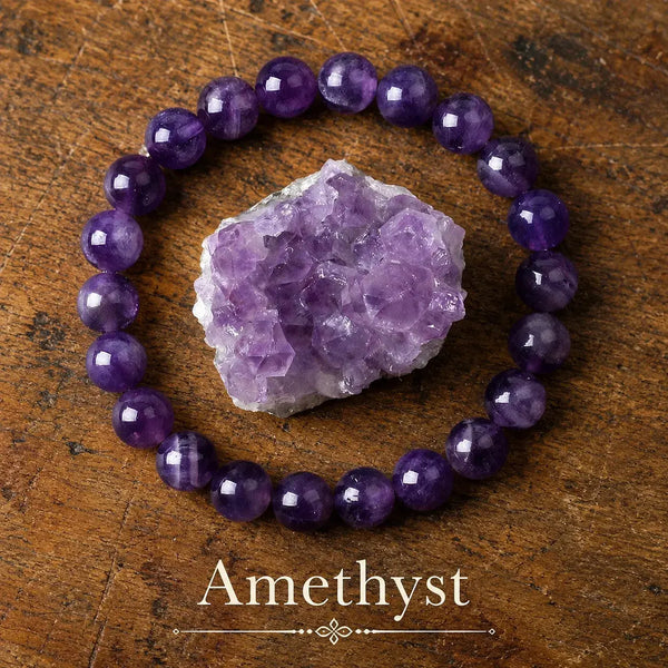 Pulsera elástica de cuentas redondas de amatista morada de distintas intensidades, junto a una geoda de amatista sobre madera