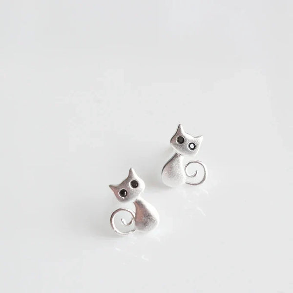 Pendientes de botón muy pequeños con la silueta de un gato sentado y la cola enroscada, en acabado plateado mate con los ojos en negro
