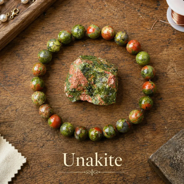 Pulsera elástica de cuentas redondas de unakita verde musgo con zonas de color salmón, junto a un trozo en bruto de la piedra