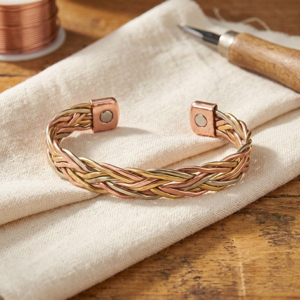 Pulsera rígida tejida en espiga con tres hilos en tono cobre rosado, dorado cálido y crema, con remates cuadrados
