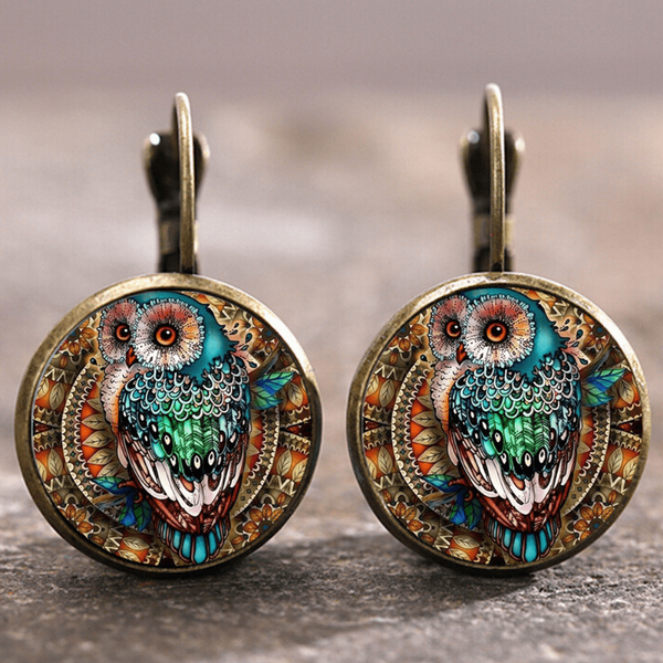 Pendientes redondos en tono bronce con un cristal abombado que lleva impreso un búho de colores verdes, naranjas y azules, con cierre de palanca